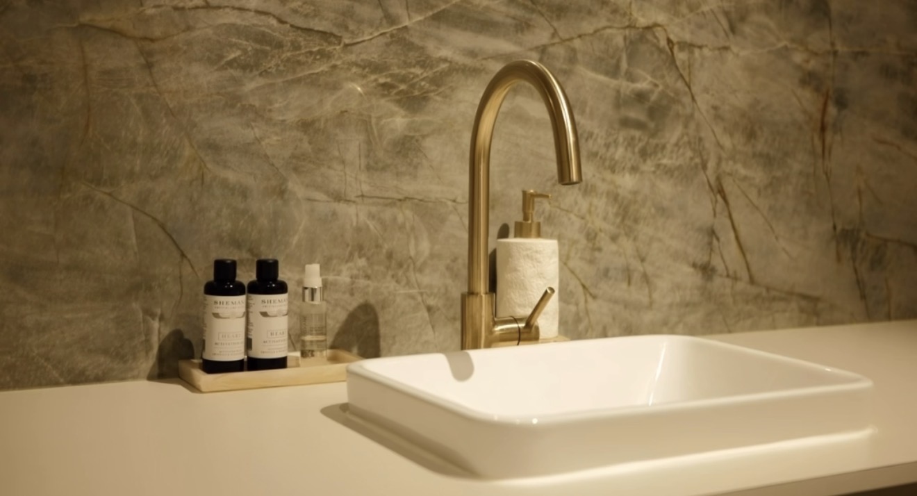 Basin detail at SSKIN Robina: brushed gold tap, marble wall and skincare bottles on a timber tray